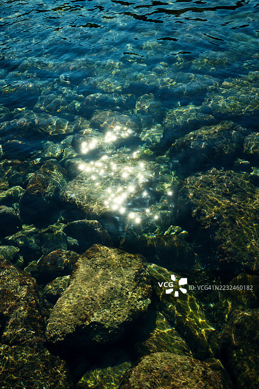 阳光在清澈的地中海水面上照射在岩石上形成的倒影图片素材