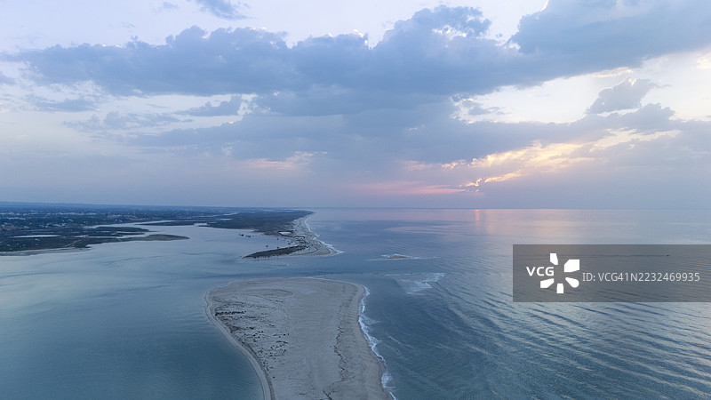 海岸高处的视角，沙滩被宁静的海水环绕，映照出清晨柔和的色调。天空中点缀着几朵云彩。图片素材