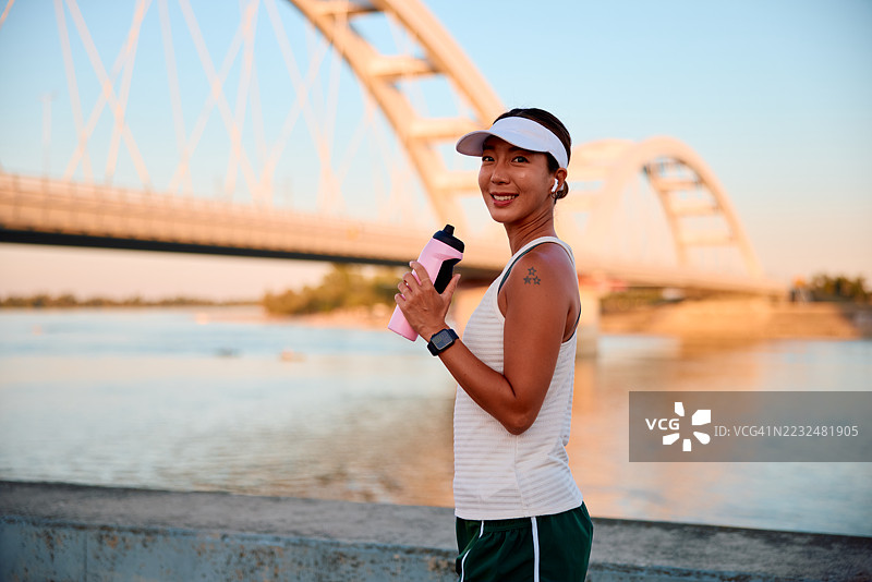年轻的女运动员在河边和桥附近锻炼后喝水图片素材