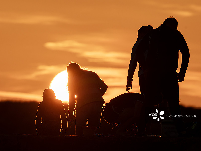 日落时分，在英国诺森伯兰郡比德内尔海港墙上的一家人正在抓螃蟹。图片素材