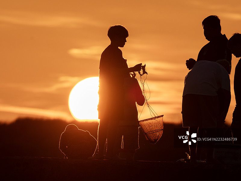 日落时分，一家人在英国诺森伯兰郡比德内尔港口墙上抓螃蟹。图片素材