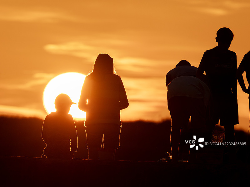 日落时分，在英国诺森伯兰郡比德内尔港的码头墙上，一家人正在抓螃蟹。图片素材