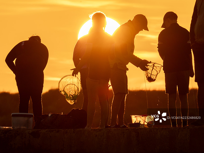 日落时分，一家人在英国诺森伯兰郡比德内尔港口墙上抓螃蟹。图片素材