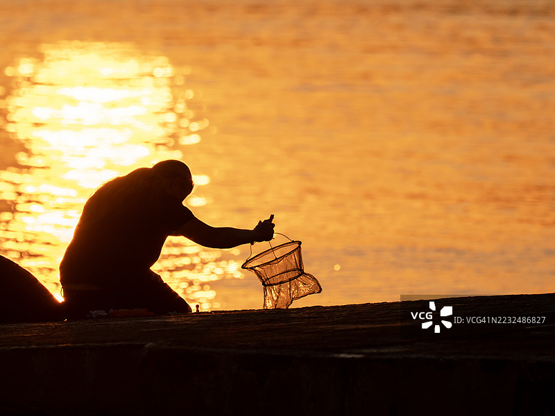 英国诺森伯兰郡比德内尔海滩，日落时分，一名男子在海港钓蟹。图片素材
