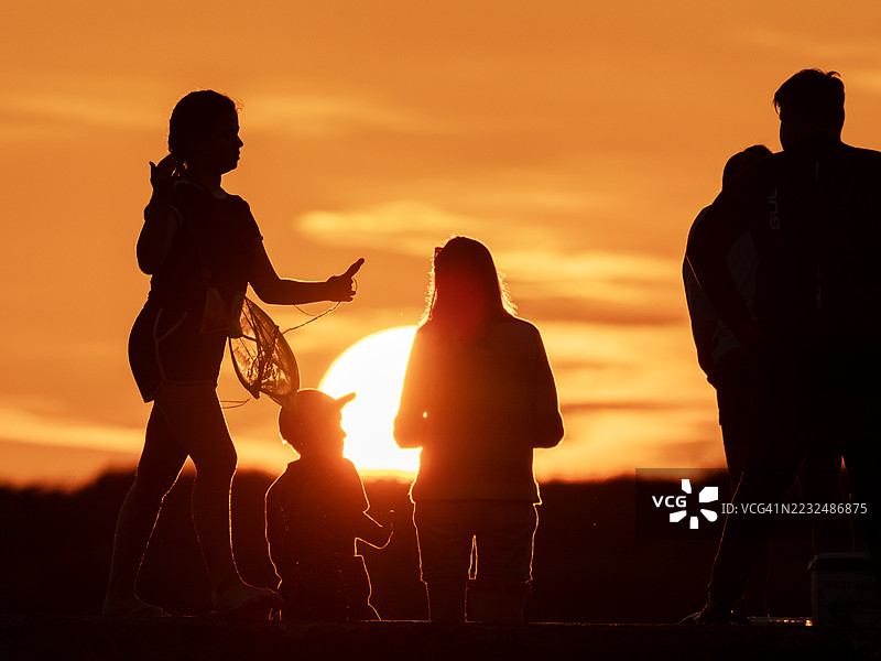 英国诺森伯兰郡比德内尔港口墙上，一家人正在日落时分钓螃蟹。图片素材