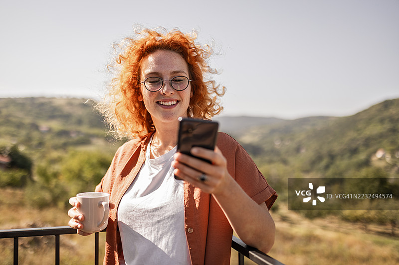 年轻女性在夏天户外放松，手里拿着咖啡和手机图片素材