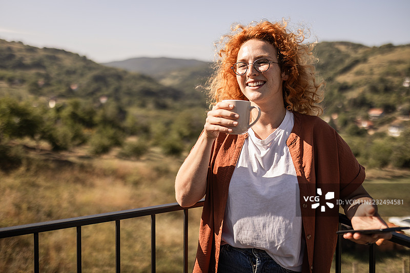 放松的女性在阳台上喝咖啡时浏览智能手机图片素材