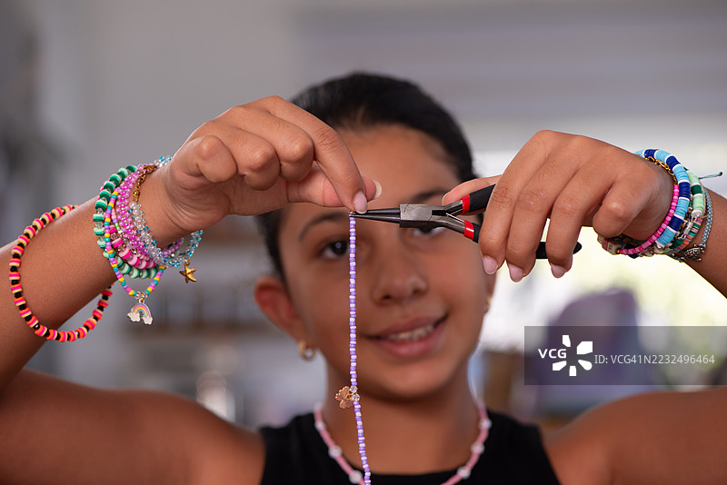 女孩用钳子制作手工串珠手链。图片素材