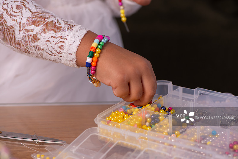 孩子的手在挑选五颜六色的珠子制作首饰。图片素材