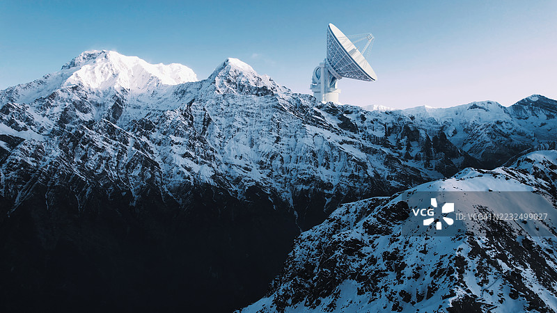 两座巨大的卫星天线位于雪山之巅，映衬着明亮的天空。图片素材