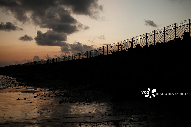 铁丝网围栏。监狱或边境围栏，带有剃刀丝，背景为日落天空。安全概念图片素材