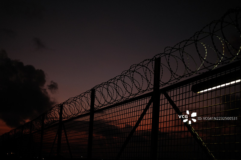 铁丝网。监狱或边境围栏，带有刀片刺网，背景为日落天空。安全概念图片素材