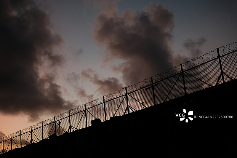 带刺铁丝网。监狱或边境围栏，带有刀片刺网，背景为日落天空。安全概念图片素材