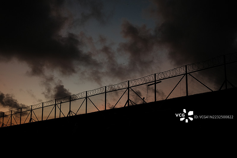 带刺的铁丝网。监狱或边境围栏，带有剃刀丝，映衬着日落天空。安全概念图片素材