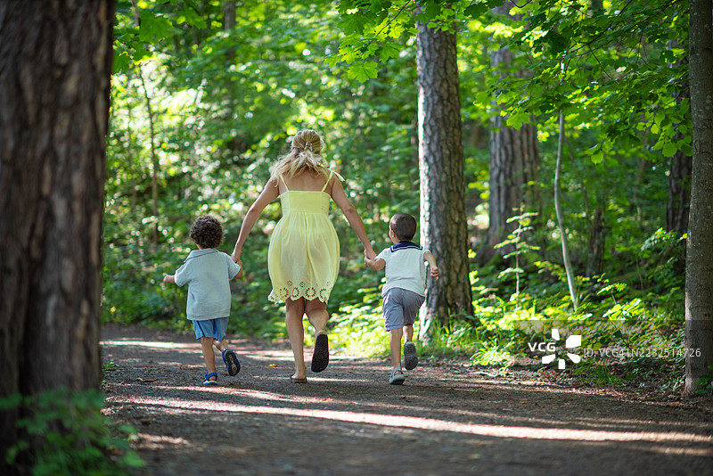 母亲与她的儿子们手牵手在森林中奔跑。图片素材