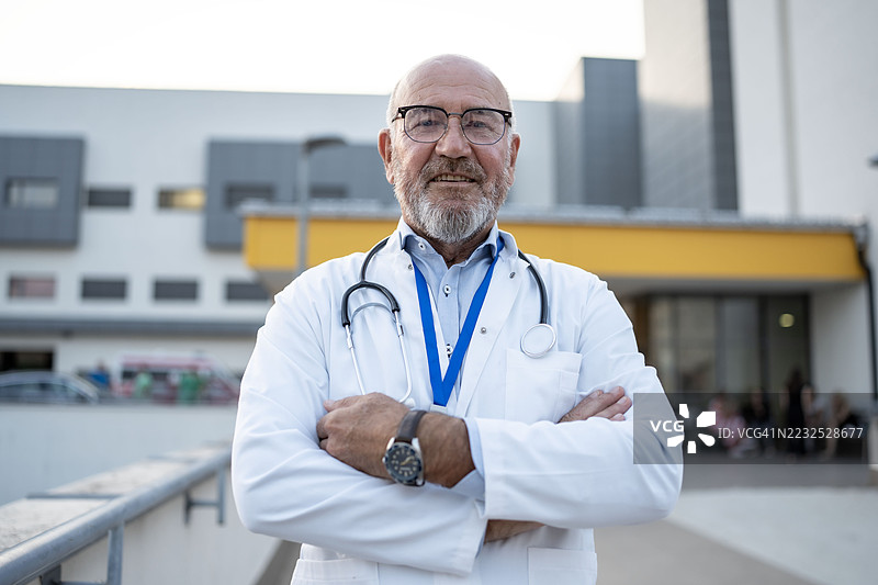 自信的资深医生站在现代医院建筑外图片素材