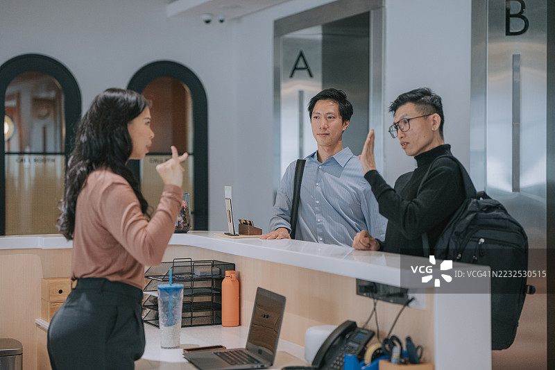 中国商务专业人士在现代办公大堂与接待员使用手语交流。图片素材