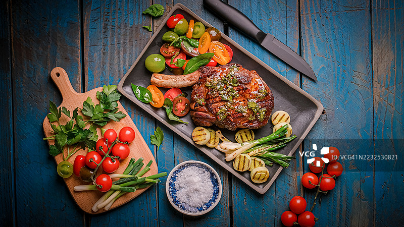 美味的烤牛排配新鲜蔬菜和香草，摆放在质朴的木桌上图片素材