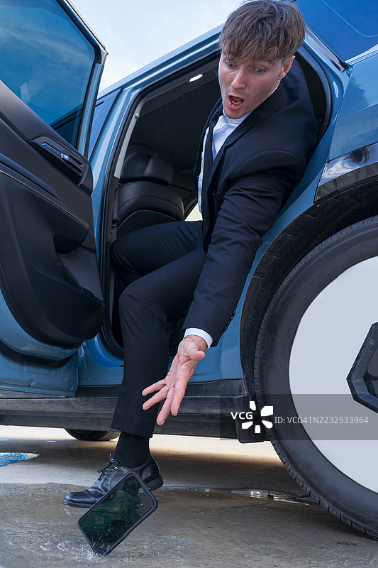 一位商人正要走出车门，他的智能手机滑落掉进了水坑里。图片素材
