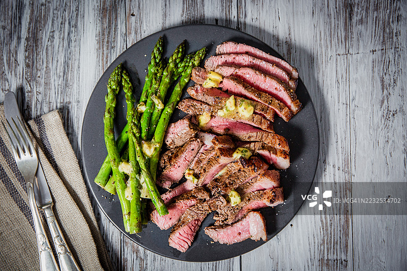 乡村木桌上的烤牛排和芦笋配蒜蓉黄油图片素材