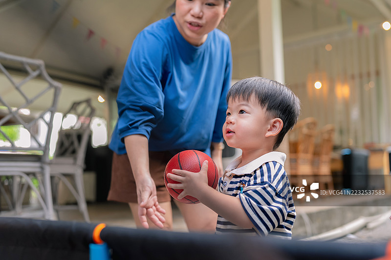 幼儿男孩在家后院与母亲练习投球，亚洲家庭的周末活动，充满乐趣和玩耍。图片素材