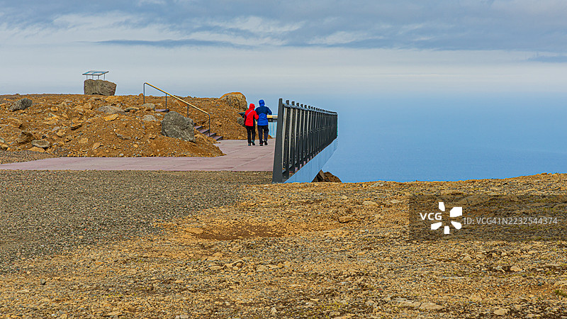 两个人在崎岖的小路上走向风景如画的海洋景观，冰岛图片素材