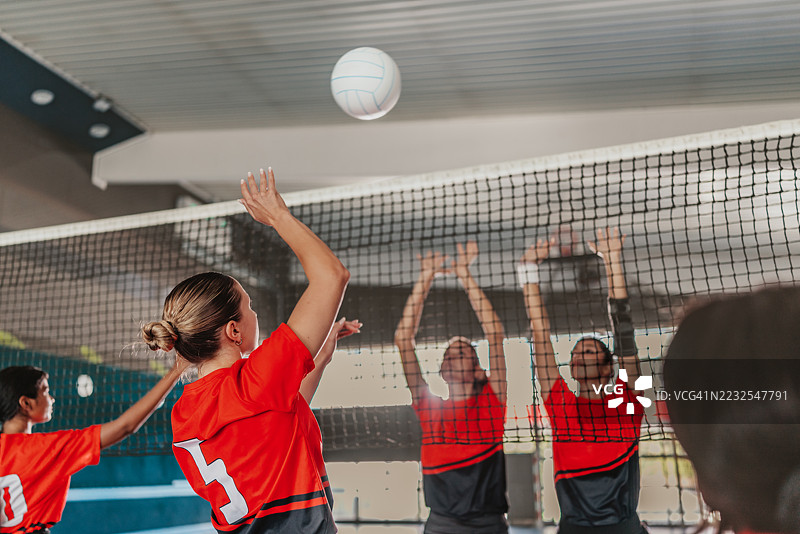 年轻女性在室内进行激烈的排球比赛，她们身着运动服，展现出团队合作与竞争精神图片素材