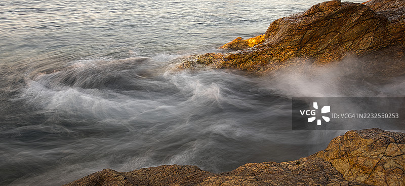 日落时分，海浪拍打着西班牙托萨德马尔的岩石海岸线图片素材
