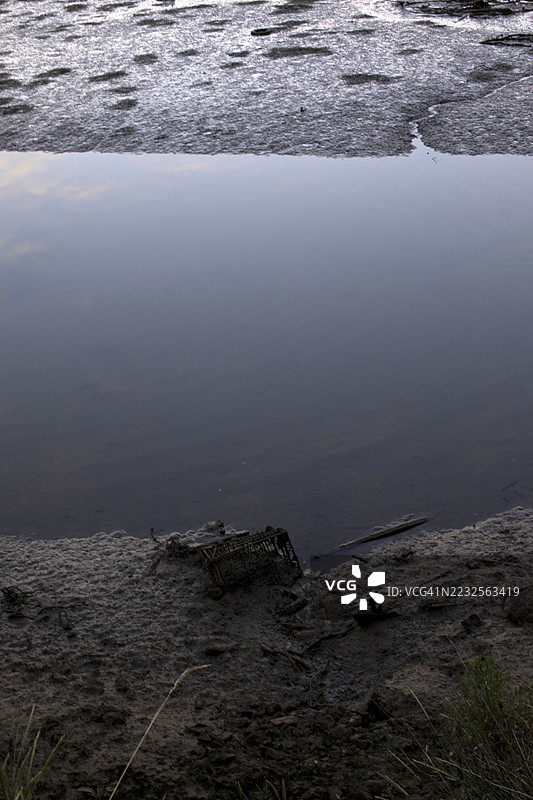 被遗弃的金属渔民笼子位于河岸，周围自然环境中有垃圾污染水源和自然。图片素材