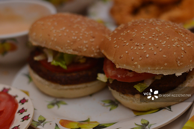 两只放有生菜和番茄的汉堡，摆放在花卉图案的盘子上图片素材
