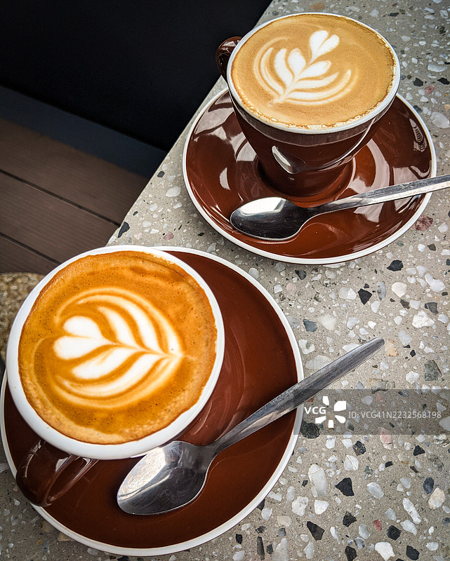 两杯带拉花的卡布奇诺放在水磨石桌子上图片素材