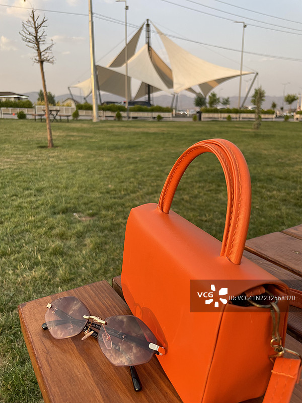 公园里木长椅上的橙色手提包和太阳镜图片素材
