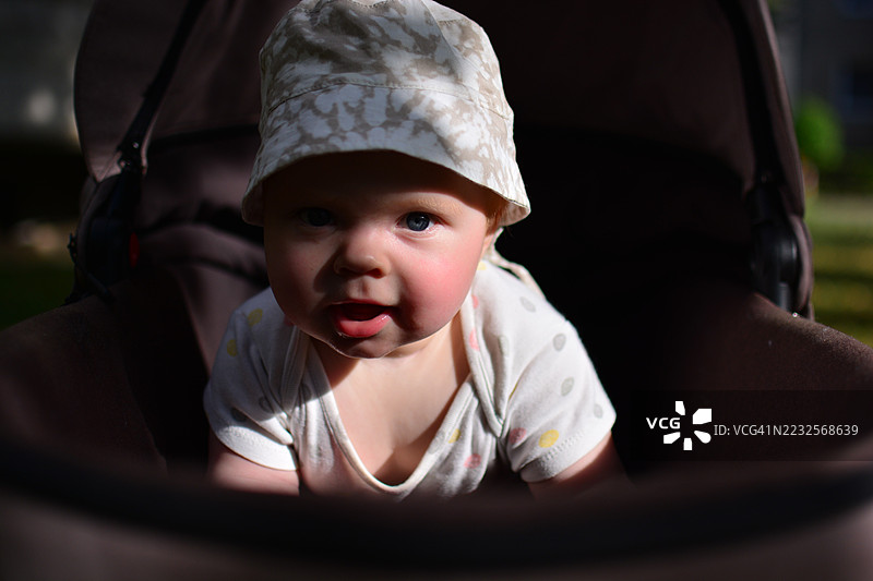 戴着帽子的婴儿女孩坐在户外的婴儿车里图片素材