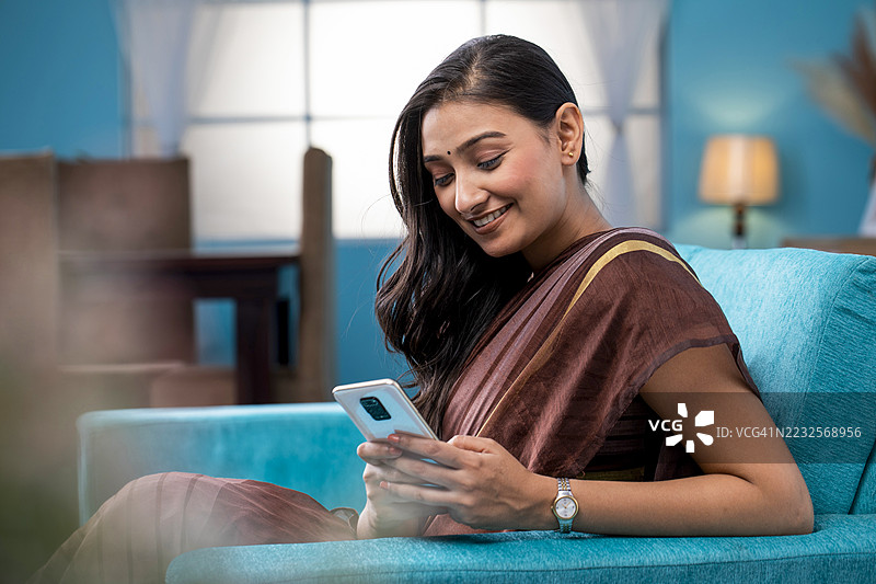 穿着传统服饰的女性在家中的沙发上使用智能手机图片素材