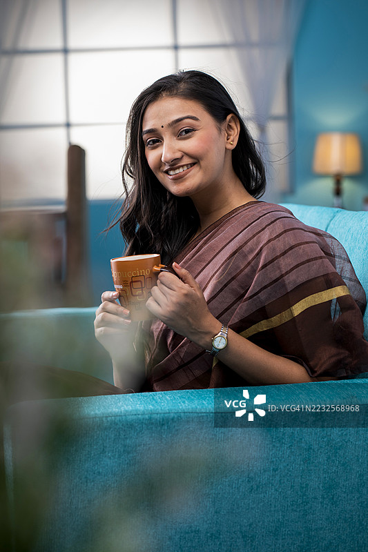 年轻女性穿着纱丽在室内享受咖啡图片素材