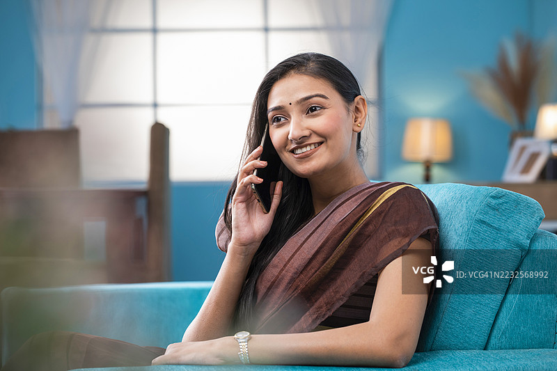 身穿传统服饰的年轻女性在家中打手机。图片素材