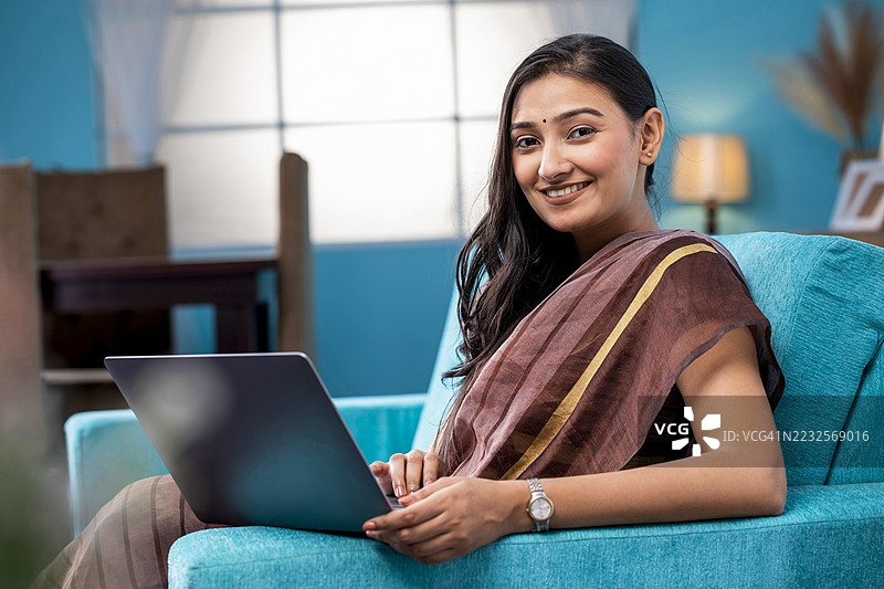 年轻的亚洲女性在室内放松，使用笔记本电脑图片素材