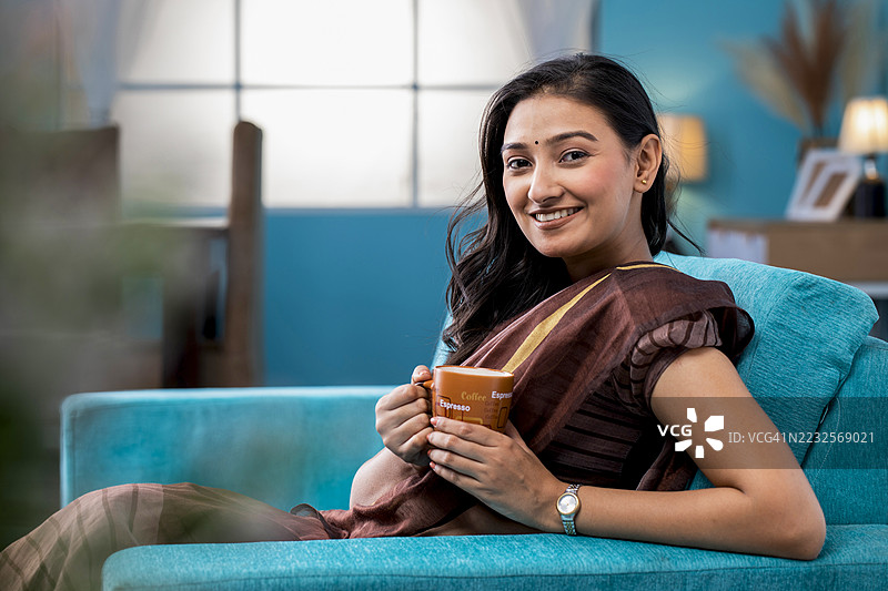 身穿传统服饰的女性在沙发上悠闲地享用咖啡图片素材