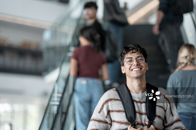 微笑的学生在现代校园环境中，背景中有多元化的同学。图片素材