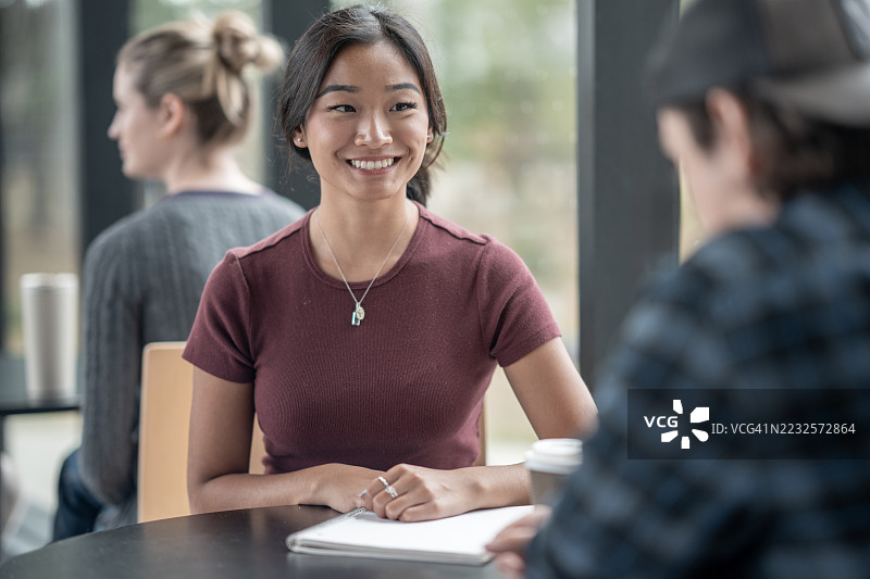 年轻女性在舒适的咖啡馆环境中与朋友聊天图片素材