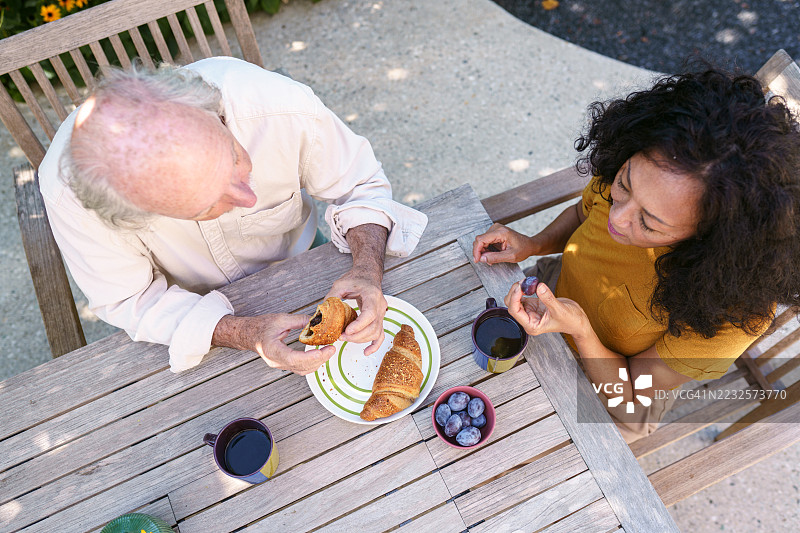 快乐的西班牙裔老年夫妇在后院享用咖啡和糕点图片素材