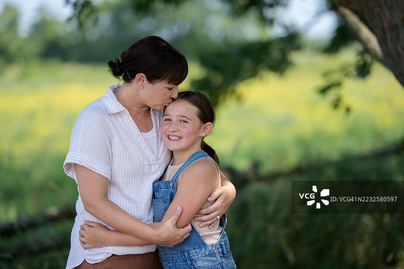 温暖的母亲在阳光明媚的绿色公园中拥抱着微笑的女儿图片素材