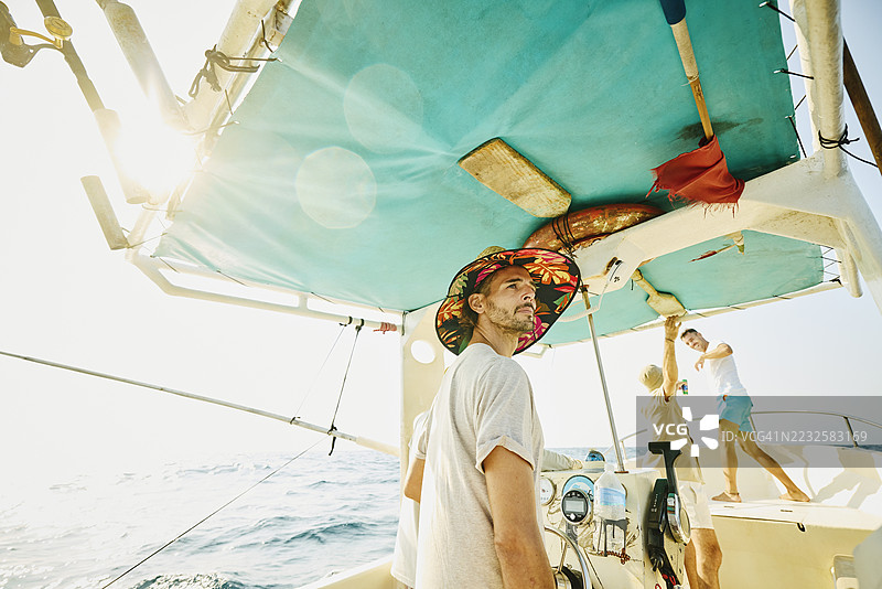 中景拍摄，男子驾驶着钓鱼船，背景中有朋友们。图片素材