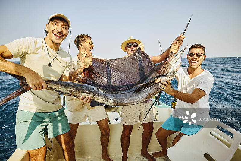 中景父亲和儿子们在船上举着刚捕获的帆船鱼图片素材