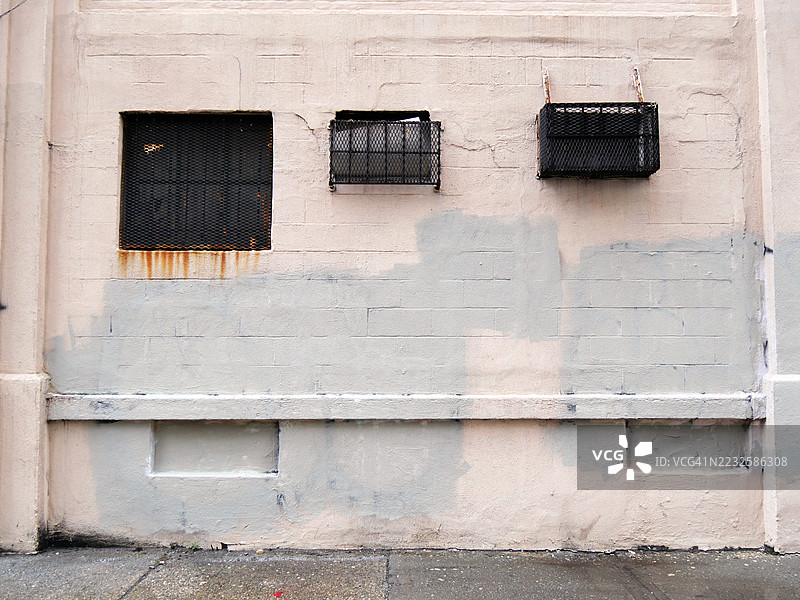 涂漆和上光的混凝土墙，带有窗户和被生锈格栅保护的空调。肮脏的水泥人行道。美国纽约州曼哈顿。阳光。自然色彩。全画幅4:3。图片素材