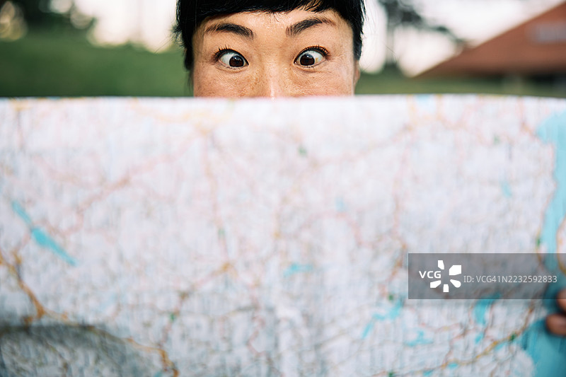 在风景如画的户外，旅行者手持地图，面露好奇表情图片素材