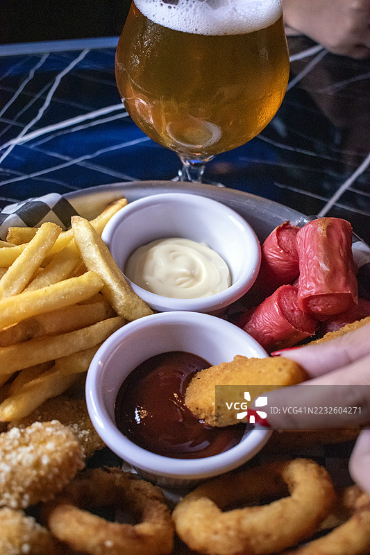薯条、香肠、马苏里拉奶酪条、洋葱圈和配料的炸鸡。快餐。美食。手工啤酒杯。图片素材