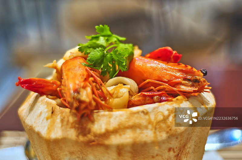 一碗盛在挖空的年轻椰子壳中的冬阴功海鲜汤特写镜头。图片素材