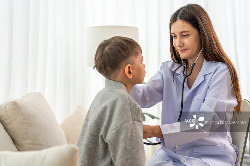 女儿科医生穿着白大褂，使用听诊器在家中为小男孩检查心跳，体现儿童健康检查、家庭护理或医生就诊、医疗咨询、儿童健康检查的概念。图片素材