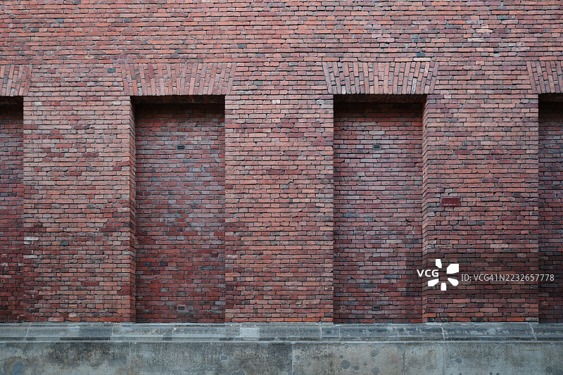 一面坐落在坚固混凝土基础上的风化红砖墙的正面视图。图片素材